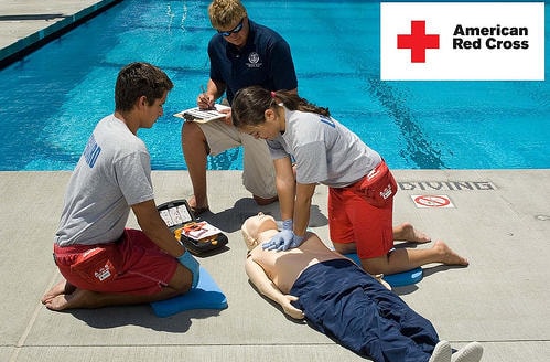 Trainees practice CPR on a manikin beside a swimming pool.